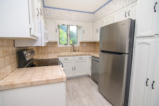 kitchen featuring sink, tile countertops, appliances with stainless steel finishes, white cabinets, and light wood-type flooring