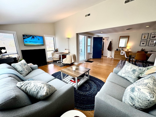 living room featuring plenty of natural light, visible vents, vaulted ceiling, and wood finished floors