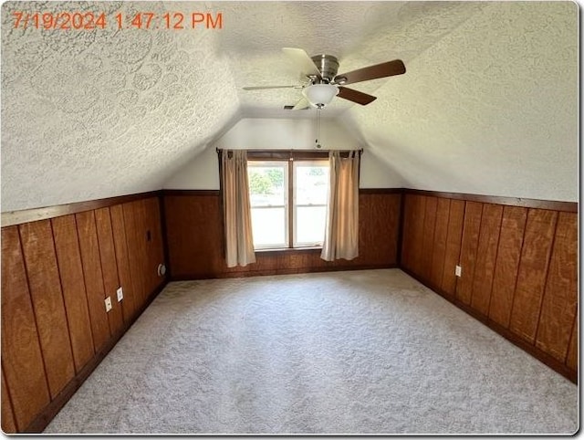 additional living space featuring ceiling fan, light colored carpet, a textured ceiling, and wooden walls