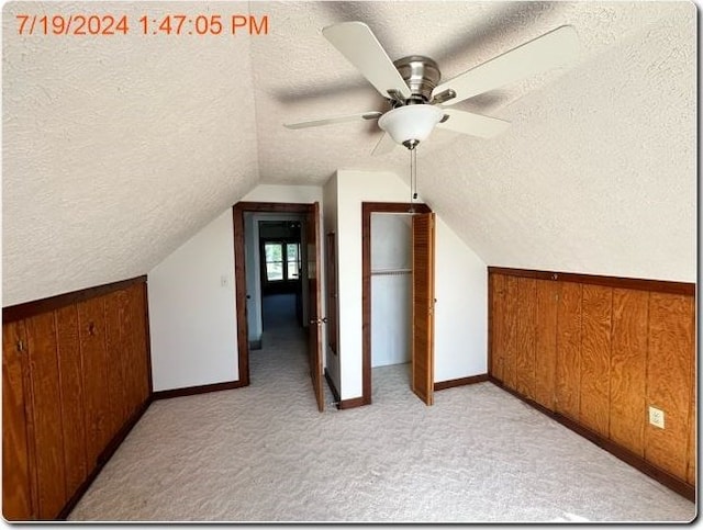 additional living space with wooden walls, ceiling fan, and a textured ceiling