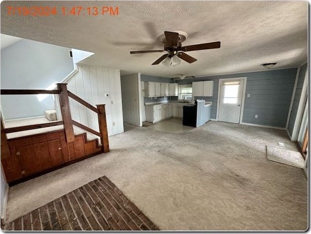 unfurnished living room featuring ceiling fan, light colored carpet, a textured ceiling, and wooden walls