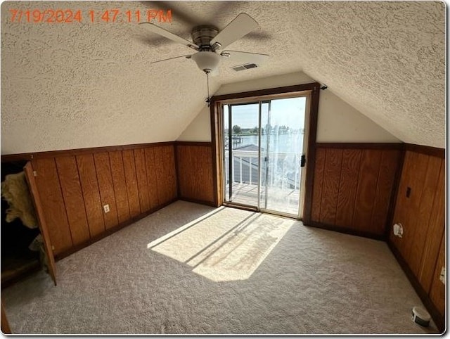 additional living space featuring light carpet, a textured ceiling, ceiling fan, and wooden walls