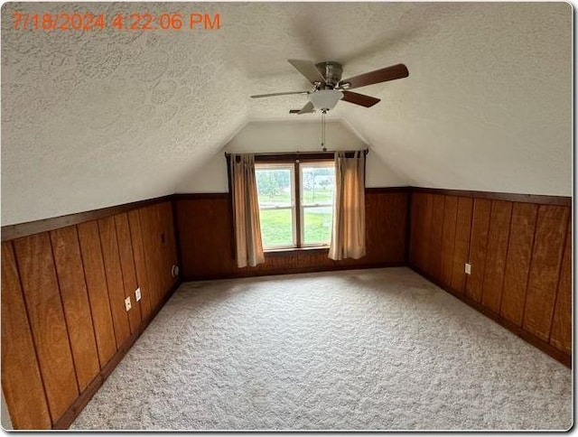 additional living space with a textured ceiling, light colored carpet, ceiling fan, and wooden walls