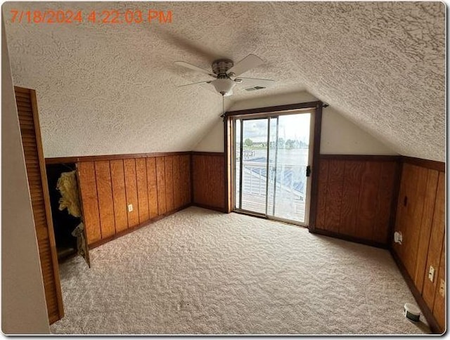 bonus room featuring ceiling fan, light carpet, vaulted ceiling, a textured ceiling, and wooden walls