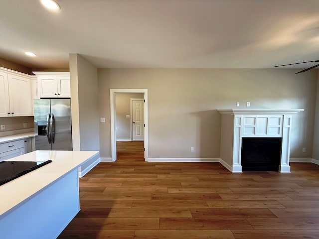 kitchen with a ceiling fan, wood finished floors, white cabinetry, a fireplace, and stainless steel fridge with ice dispenser