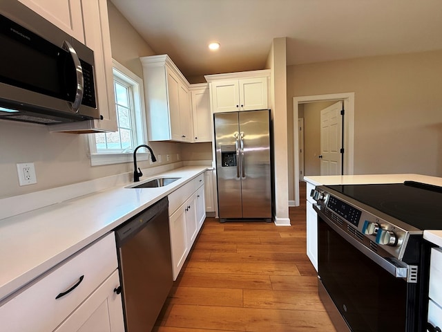 kitchen featuring light wood-type flooring, light countertops, white cabinets, stainless steel appliances, and a sink