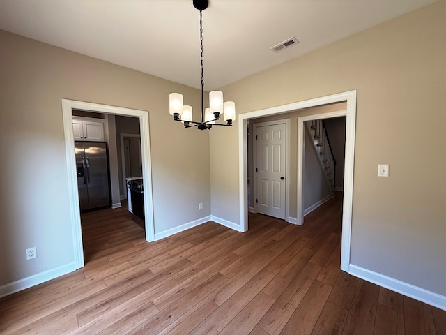 unfurnished dining area featuring stairway, baseboards, visible vents, wood-type flooring, and a notable chandelier