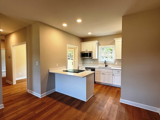 kitchen with a sink, stainless steel microwave, black electric stovetop, and white cabinets