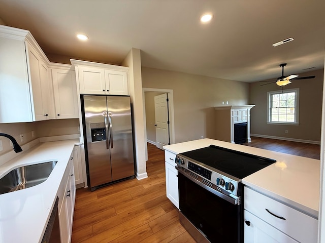 kitchen featuring visible vents, light wood-type flooring, a fireplace, stainless steel appliances, and a sink