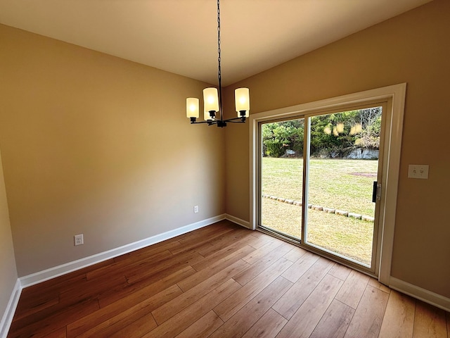 unfurnished room with a chandelier, baseboards, and wood finished floors