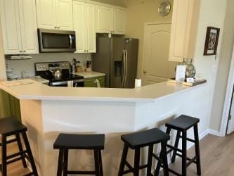 kitchen featuring white cabinets, a kitchen breakfast bar, appliances with stainless steel finishes, light hardwood / wood-style floors, and kitchen peninsula