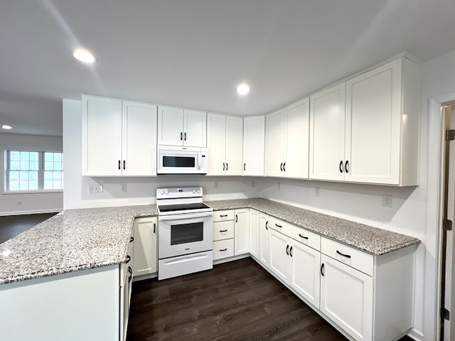 kitchen with white appliances, light stone countertops, white cabinets, dark hardwood / wood-style flooring, and kitchen peninsula