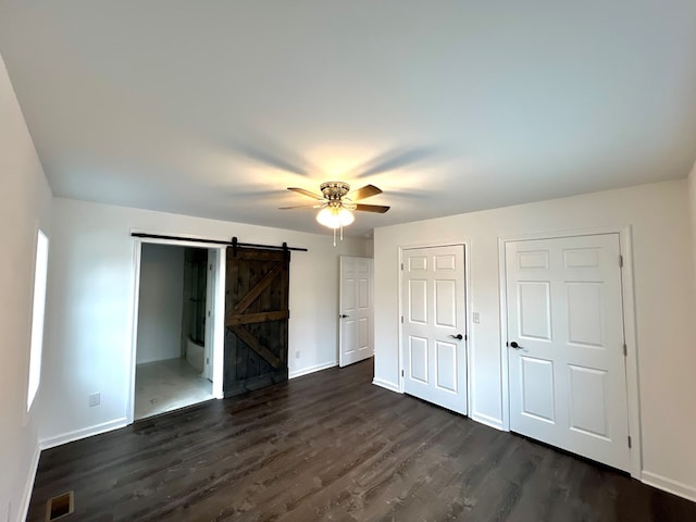 unfurnished bedroom featuring dark hardwood / wood-style floors, ceiling fan, and a barn door