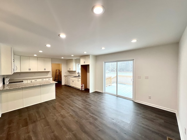 kitchen featuring dark hardwood / wood-style floors, white cabinetry, sink, light stone counters, and kitchen peninsula