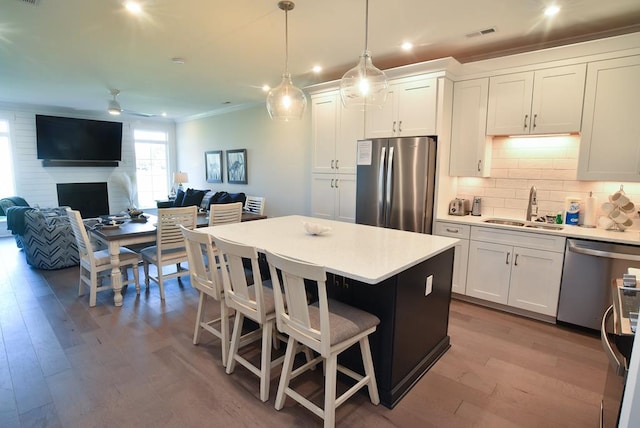 kitchen with white cabinetry, sink, stainless steel appliances, decorative light fixtures, and a kitchen bar