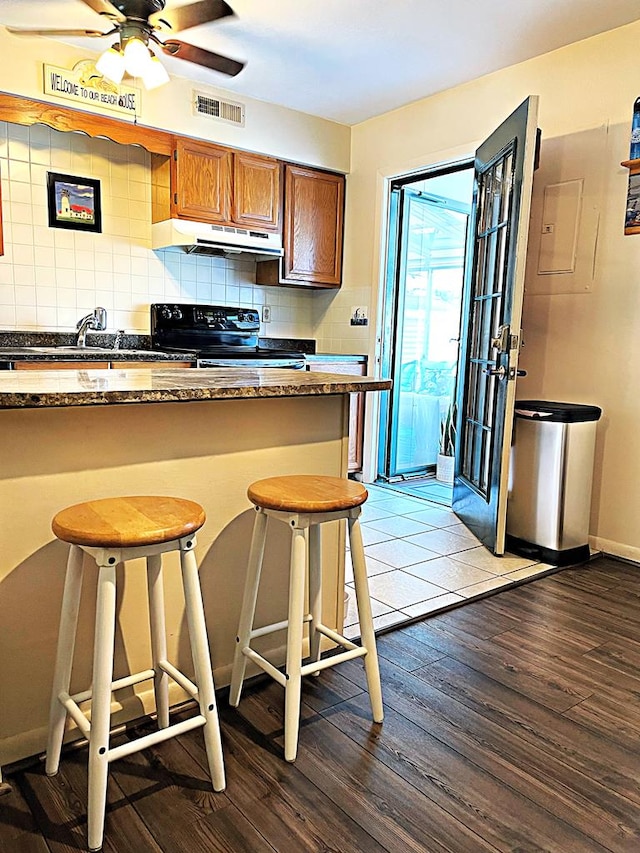 kitchen with electric range, a kitchen breakfast bar, dark hardwood / wood-style flooring, and tasteful backsplash