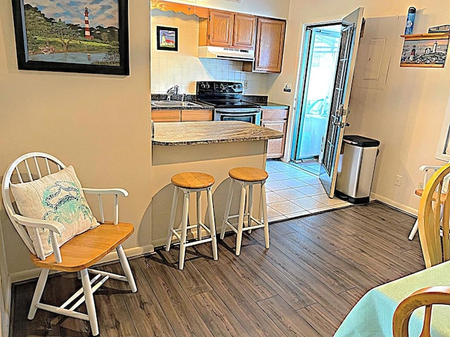 kitchen featuring black / electric stove, sink, tasteful backsplash, light hardwood / wood-style floors, and a kitchen bar