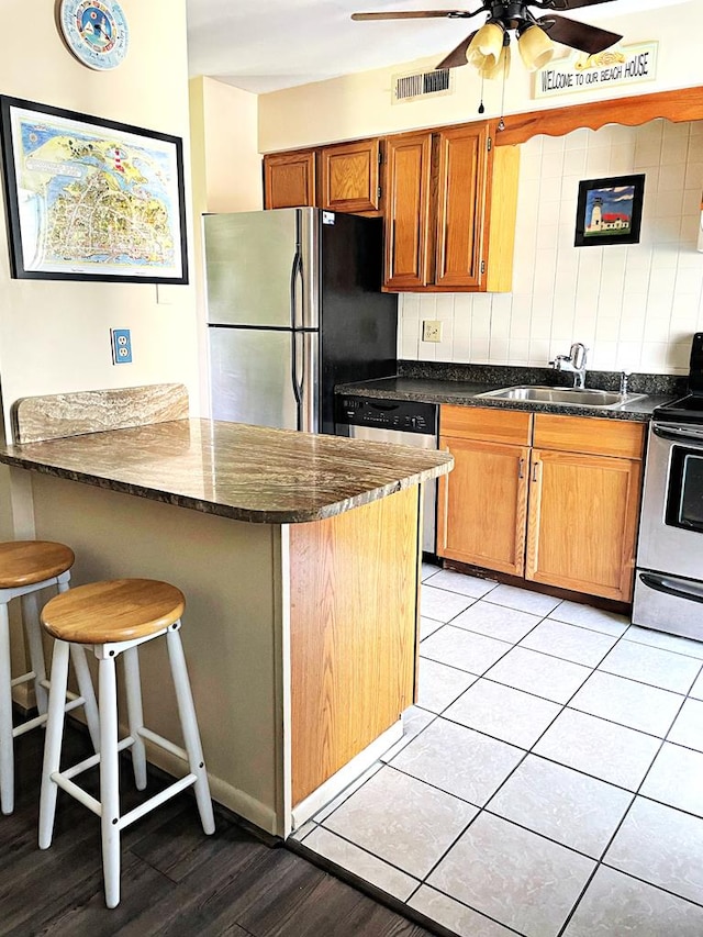 kitchen with a breakfast bar, sink, ceiling fan, dark stone countertops, and stainless steel appliances