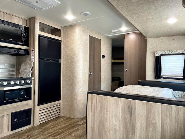 kitchen with a textured wall, dark wood-style flooring, range hood, a textured ceiling, and black appliances