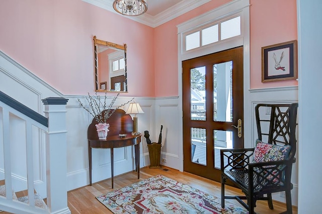 entryway with a notable chandelier, wood finished floors, wainscoting, a decorative wall, and ornamental molding