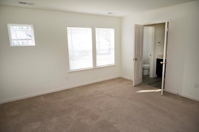 unfurnished bedroom featuring multiple windows, ensuite bath, and carpet floors