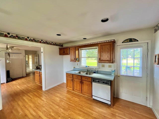 kitchen with a sink, dishwasher, light countertops, brown cabinetry, and light wood-type flooring