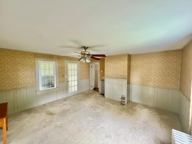 unfurnished room with a ceiling fan, wainscoting, and wallpapered walls