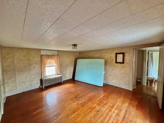 spare room featuring wood-type flooring, baseboards, and radiator heating unit