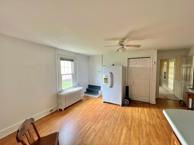 bedroom featuring radiator, baseboards, white refrigerator with ice dispenser, and light wood-style flooring