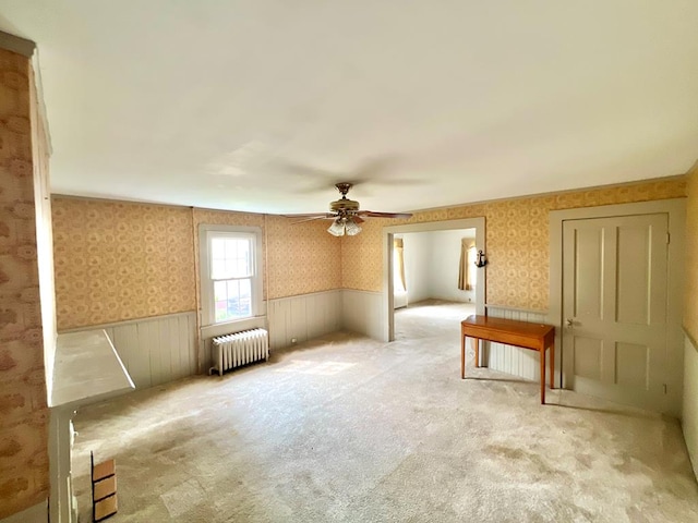spare room with wallpapered walls, ceiling fan, radiator, and a wainscoted wall
