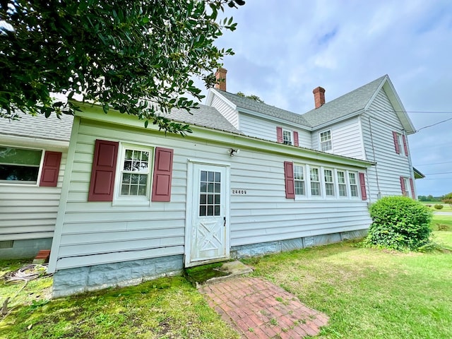 back of house featuring a lawn and a shingled roof