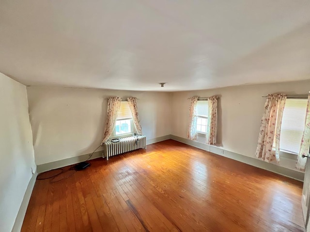 empty room featuring baseboards, radiator, and light wood finished floors