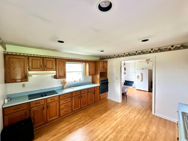 kitchen featuring black appliances, light countertops, under cabinet range hood, and brown cabinets