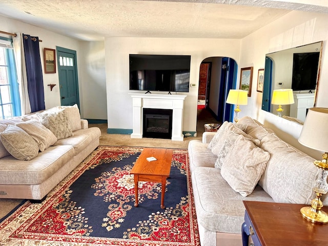 6136 Maddox Blvd, Chincoteague, VA 23336 - living room featuring baseboards, carpet floors, arched walkways, a textured ceiling, and a glass covered fireplace