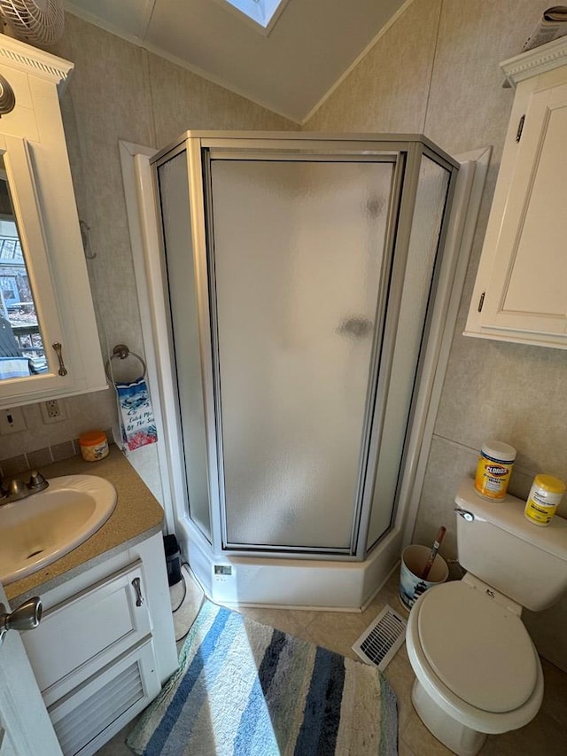 bathroom with vanity, tile patterned floors, vaulted ceiling with skylight, toilet, and a shower with shower door