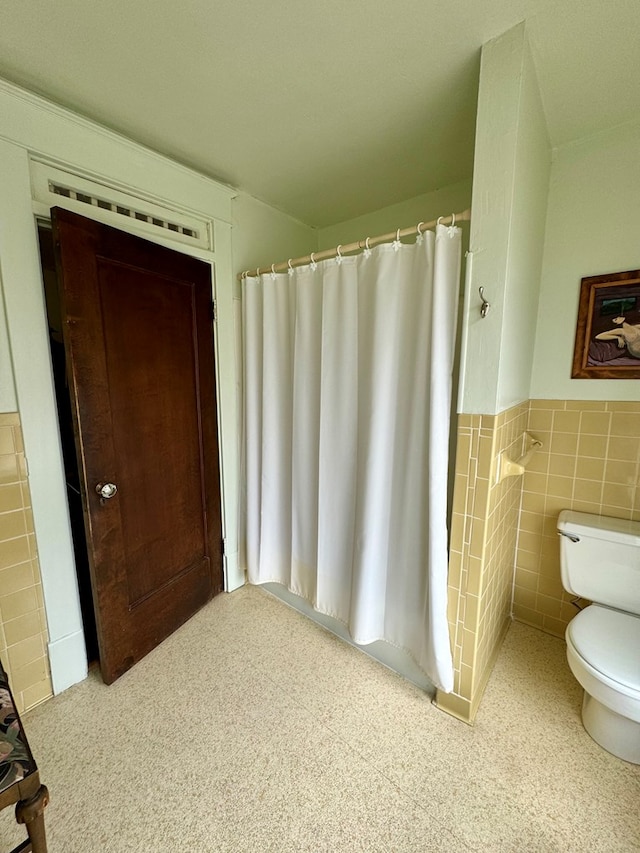 bathroom with a shower with curtain, toilet, and tile walls