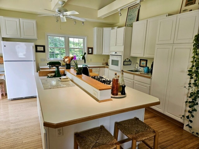 kitchen featuring sink, light hardwood / wood-style floors, white appliances, a kitchen bar, and white cabinets