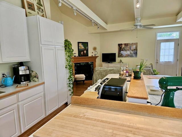 kitchen with rail lighting, beam ceiling, a fireplace, hardwood / wood-style floors, and white cabinetry