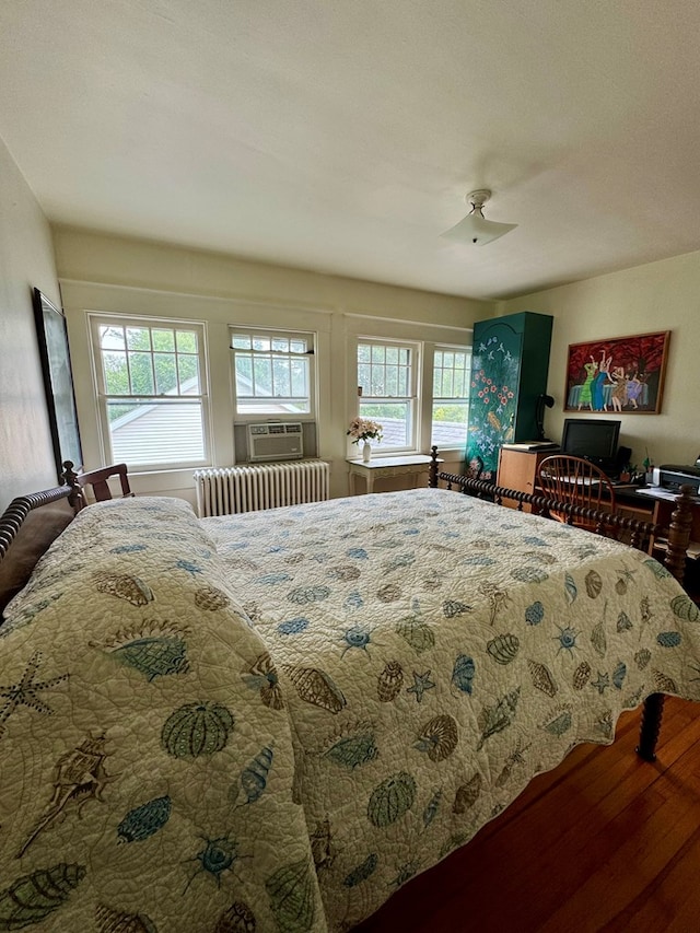 bedroom featuring radiator, hardwood / wood-style flooring, ceiling fan, and cooling unit