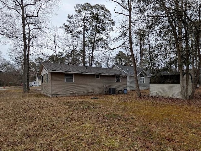 rear view of house with central AC unit and a lawn