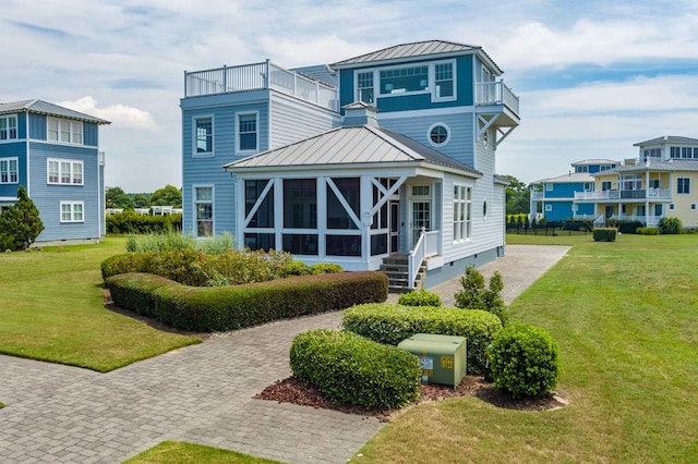 back of property featuring metal roof, a standing seam roof, a balcony, and a lawn