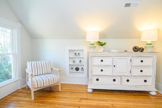 living area with built in shelves, light hardwood / wood-style flooring, and vaulted ceiling