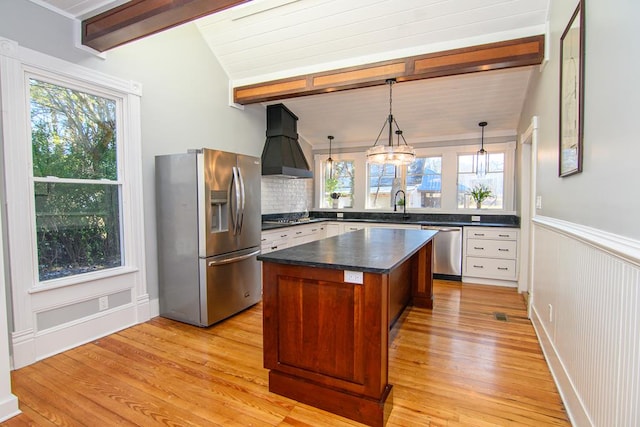 kitchen with light wood-type flooring, custom range hood, stainless steel appliances, a kitchen island, and hanging light fixtures