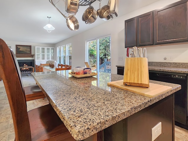 kitchen with dark brown cabinetry, light stone counters, dishwasher, and a kitchen island