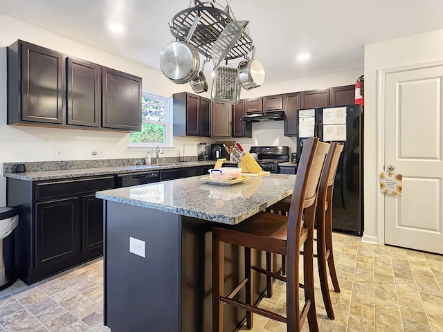 kitchen featuring dark brown cabinetry, sink, a kitchen bar, a kitchen island, and black appliances