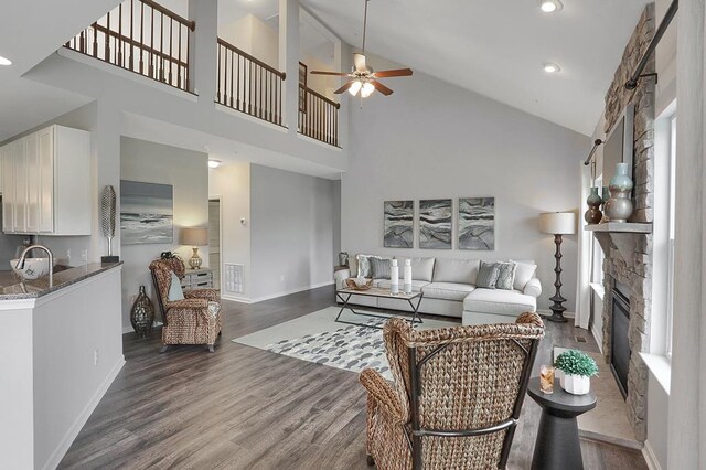 living room featuring dark hardwood / wood-style flooring, high vaulted ceiling, a healthy amount of sunlight, and a stone fireplace