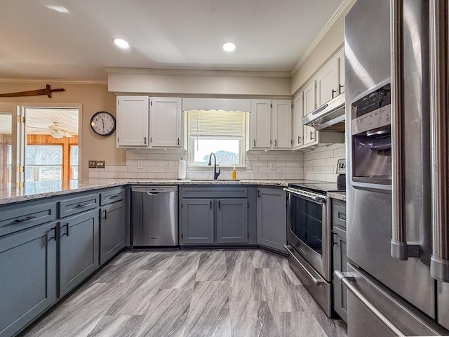 kitchen featuring under cabinet range hood, a sink, gray cabinets, and appliances with stainless steel finishes