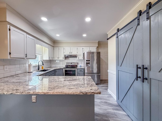 kitchen featuring crown molding, appliances with stainless steel finishes, a barn door, under cabinet range hood, and a sink