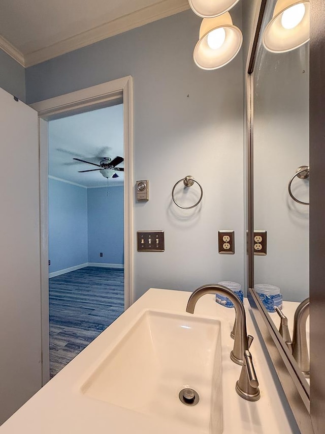 bathroom with a ceiling fan, a sink, crown molding, and wood finished floors