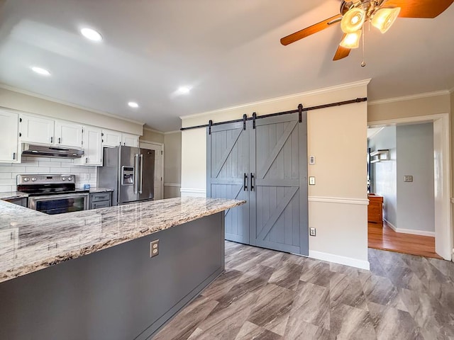 kitchen with a barn door, under cabinet range hood, appliances with stainless steel finishes, and light stone countertops